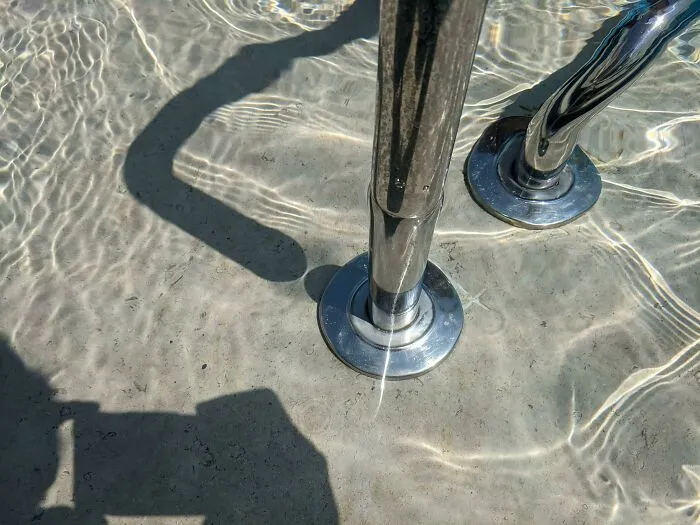 Shadows cast by a metal pool ladder on water creating cool and interesting visual effects on the pool floor.