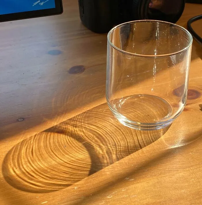 Glass casting cool, interesting shadow patterns on a wooden surface in natural sunlight.