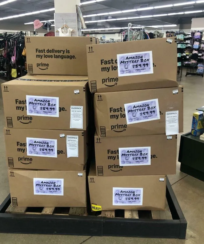 Stack of Amazon mystery boxes priced at $59.99 each displayed on a pallet in a thrift store setting.