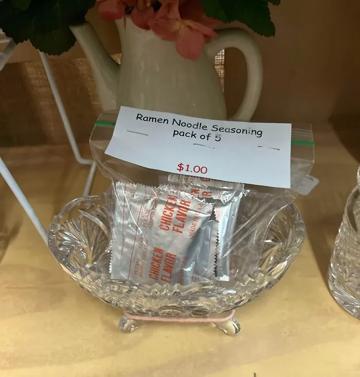 Clear glass dish holding a plastic bag of ramen noodle seasoning packs priced at one dollar in a thrift store display.