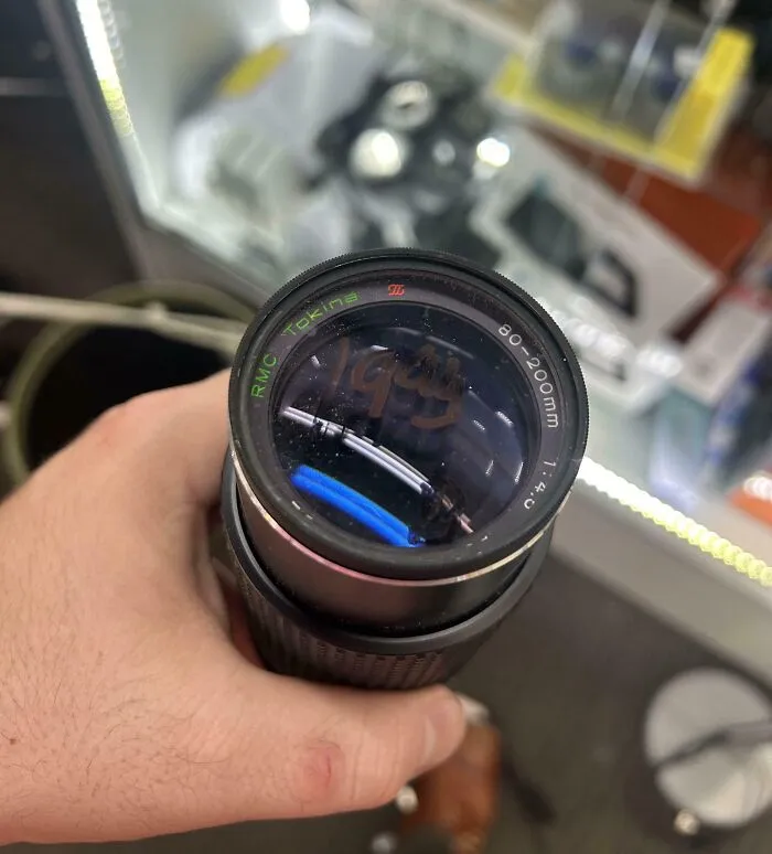 Hand holding a vintage camera lens marked 1994 found at a thrift store, showcasing a ridiculous thrift store find.