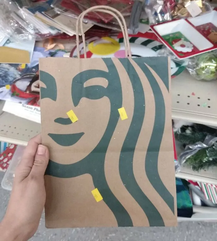 Hand holding a thrift store paper bag with a face design and yellow price stickers, found something ridiculous at the thrift store.