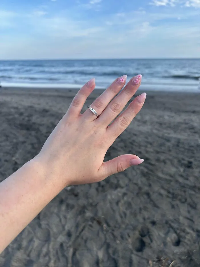 Hand with floral nail art and diamond ring displayed on a beach background symbolizing inspiring moments despite fear of flying.