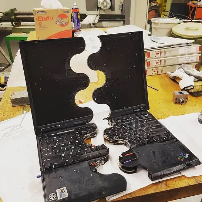 Broken laptop split in puzzle-shaped halves on a workbench, humorously illustrating absurd internet lies concept.