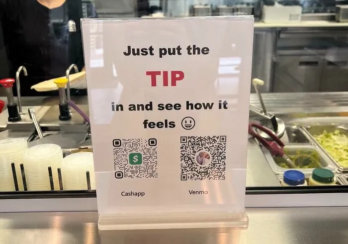 Sign at counter with QR codes for tipping via Cashapp and Venmo, highlighting ridiculous tipping culture in restaurants.