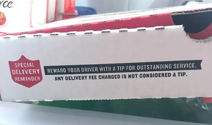 Pizza box with a delivery reminder urging customers to tip drivers, highlighting the ridiculous tipping culture trends.