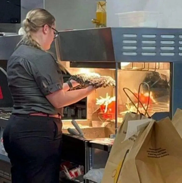 Woman working in a kitchen handling food near a fryer, illustrating the theme of traumatizing the next generation in a stressful job.