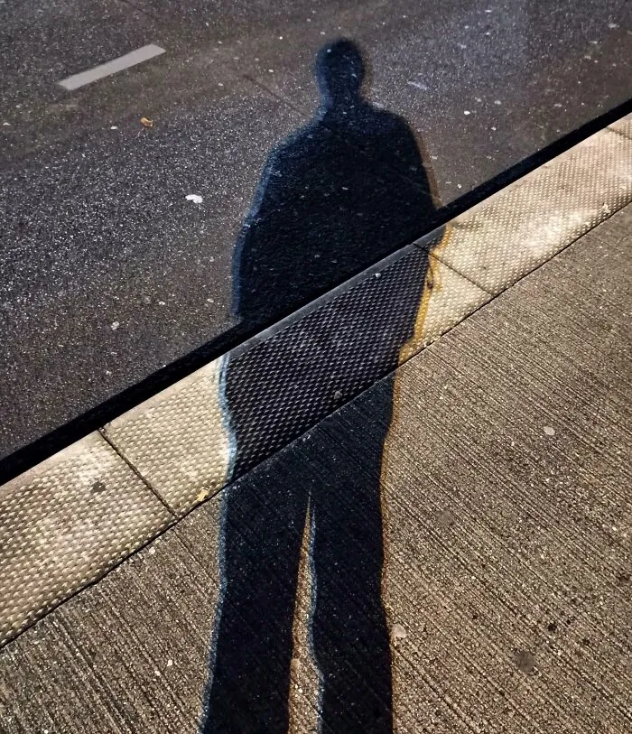 Shadow of a person standing on a textured sidewalk and road, showcasing cool and interesting shadow effects.