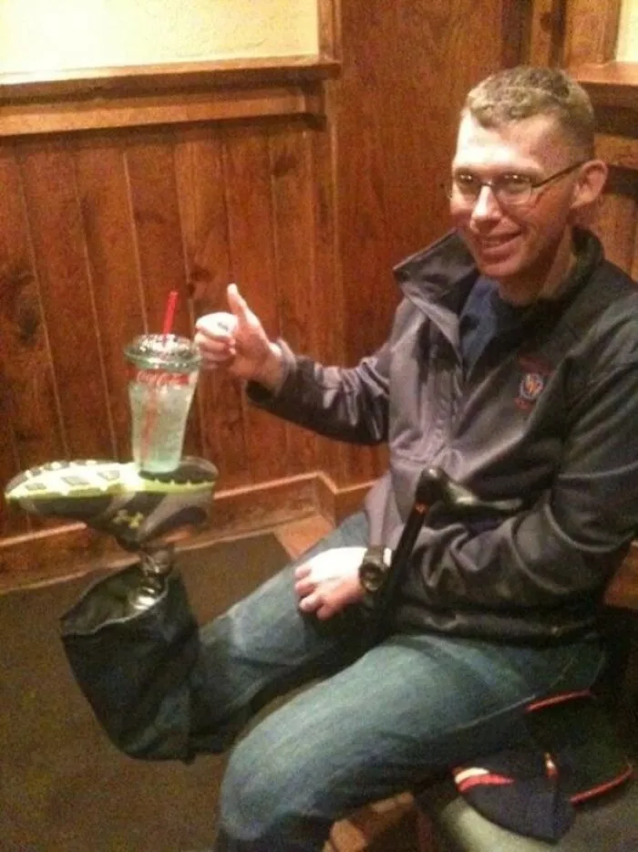 Hombre sonriente con prótesis en la pierna sosteniendo vaso en el pie en una escena divertida para hacerte reír.