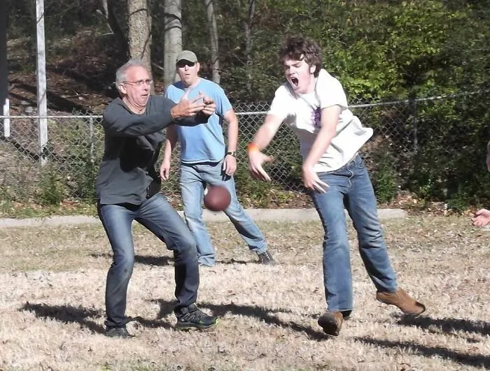 Hombres y adolescentes jugando al fútbol americano de forma divertida y espontánea en un parque al aire libre.