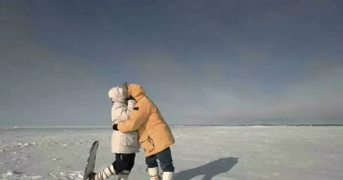 Two people dressed in winter clothing embracing on a snowy landscape representing fascinating and interesting facts content.