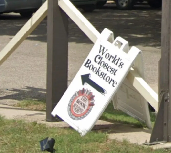 Signboard leaning against a fence pointing to the world's closest bookstore, found in shenanigans captured on Google Maps.