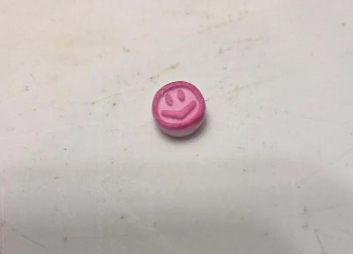Small pink mystery object with a smiley face design resting on a worn white surface, part of online group recognition.