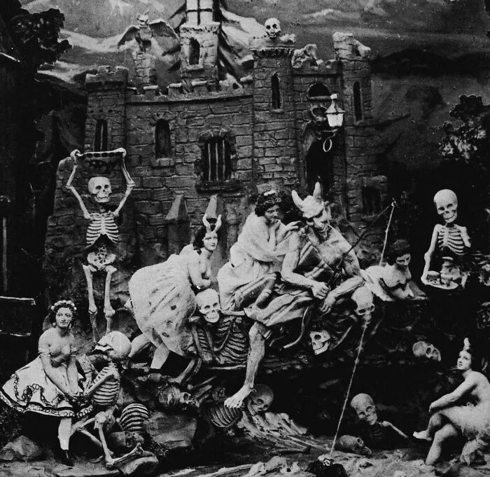 Escena inquietante del pasado con esqueletos y figuras fantásticas frente a un castillo antiguo en blanco y negro.