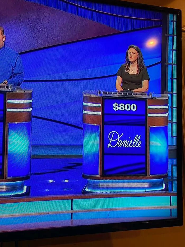 Contestant standing at a game show podium with perfect handwriting displaying the name Danielle in elegant script.