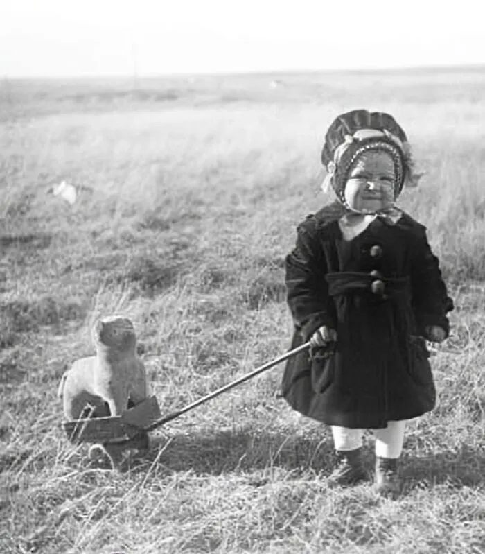 Around 1910 Near Williston, North Dakota, A Young Girl Stands In A Meadow Pulling A Toy Dog In A Two-Wheeled Cart