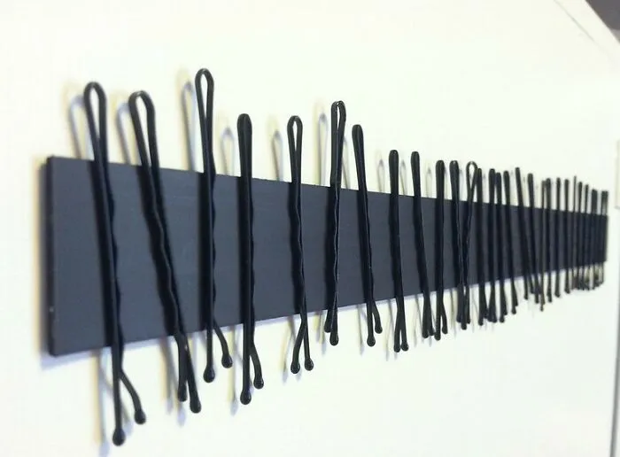 Row of black bobby pins clipped onto a black strip mounted on a white wall, illustrating pregnancy and twins concept.