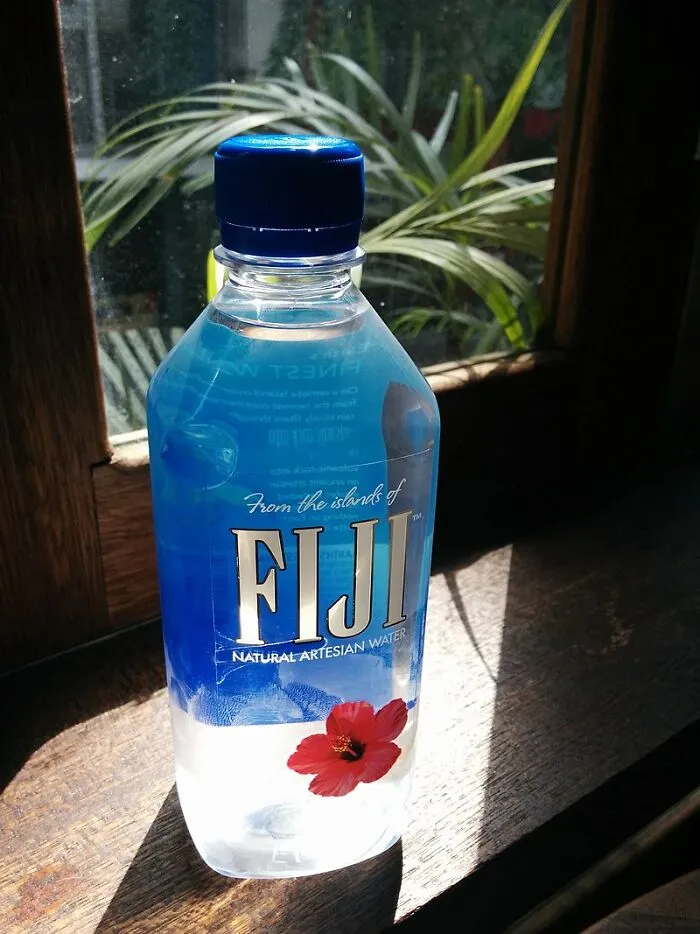 Plastic bottle of Fiji water on a wooden windowsill with natural light, illustrating out-of-touch rich people flaunting wealth.