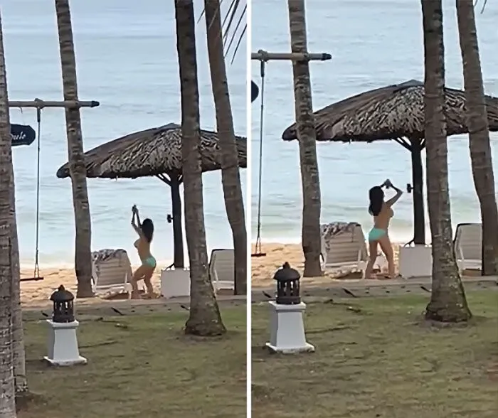 Influencer vergonzosa en bikini tomando fotos en la playa cerca de palmeras y sombrilla de paja junto al mar.