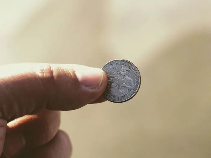 Close-up of hand holding a US quarter dollar coin symbolizing financial decisions and biggest life mistakes.