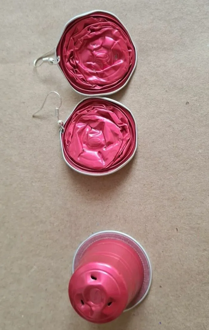 DIY craft project showing earrings made from crushed pink coffee capsules on a plain background.