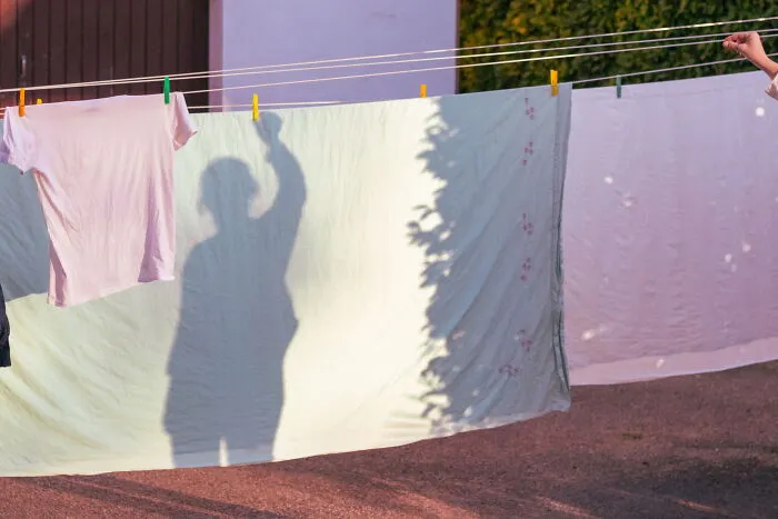 Shadow of a person raising an arm seen on laundry hanging on a clothesline in a perfectly timed street photo.