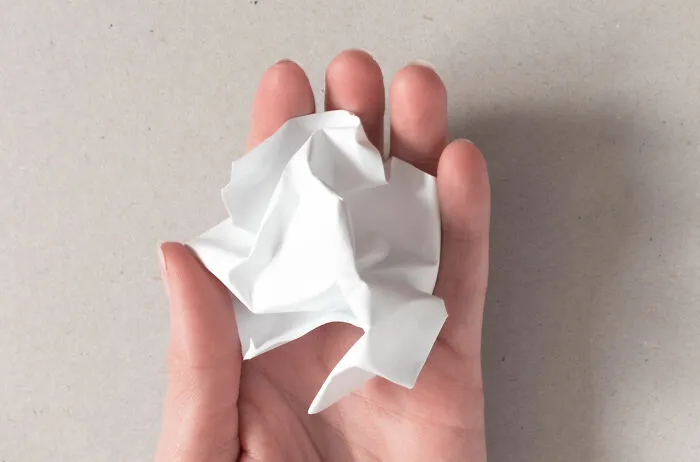 Hand holding a crumpled piece of white paper, illustrating unexpected problems for airport security checks.