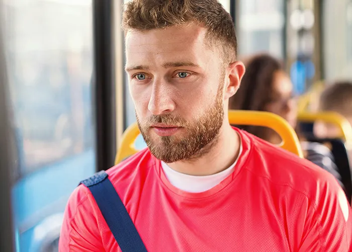 Young man in a red shirt looking pensive while riding public transport, capturing the bizarre and surreal commute experience.