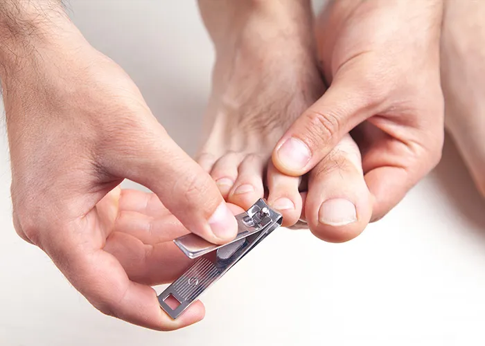 Person using metallic nail clipper to trim toenails, capturing a close-up moment of personal care and hygiene.