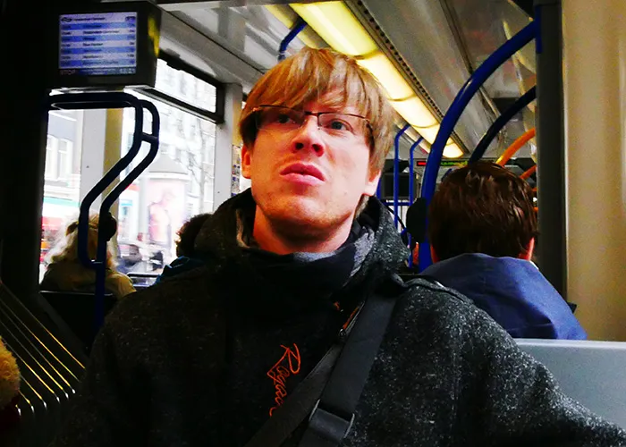 Young man with glasses looking uneasy while sitting on public transport during a busy urban commute experience