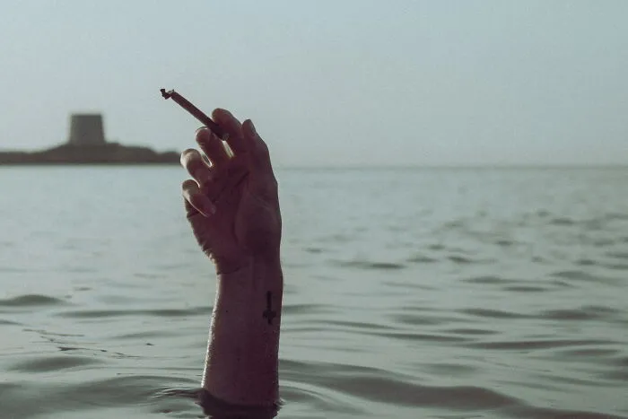 Hand emerging from water holding a burning cigarette, captured in a perfectly-timed street photo by Luca Regoli.
