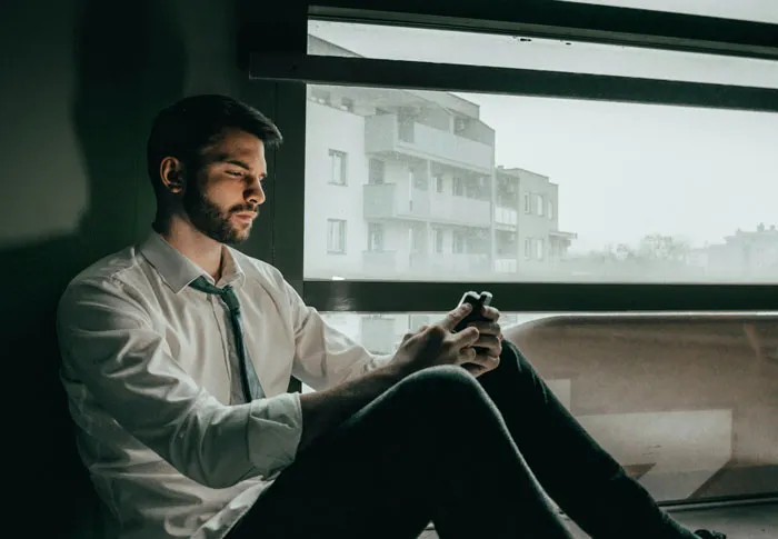Young man in a white shirt sitting by a window, reflecting deeply on the biggest mistake of his life.