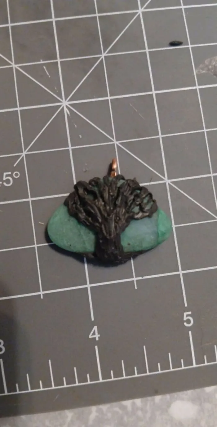 Small handmade pendant with a tree design on a green stone, displayed on a craft cutting mat, DIY project craft shaming.