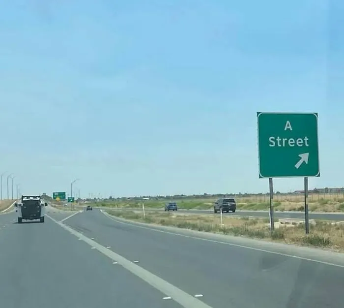Road sign for A Street exit on a clear highway, showing one of the hilarious signs adding chaos to the world.