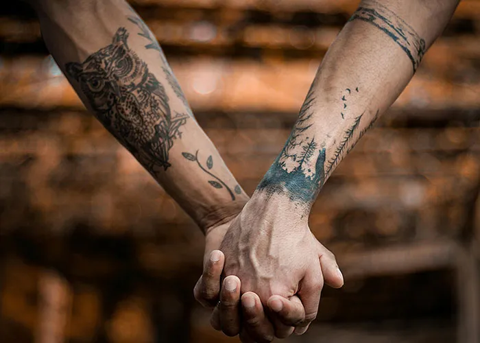 Close-up of two tattooed arms holding hands, symbolizing relationships and engagement stories involving betrayal and trust.