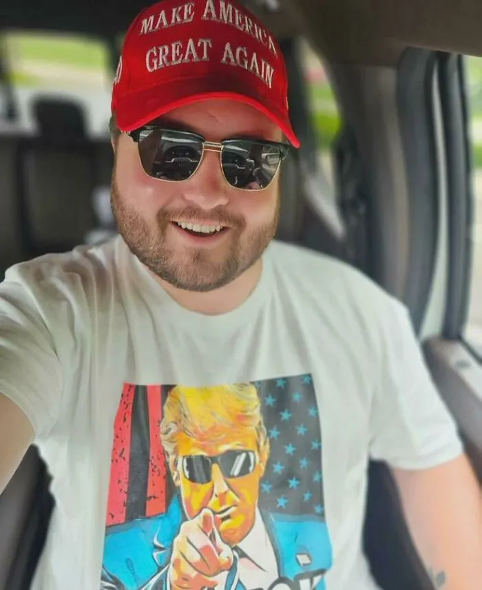 Man wearing a red MAGA hat and sunglasses smiling inside a car, highlighting a traumatizing generation theme.