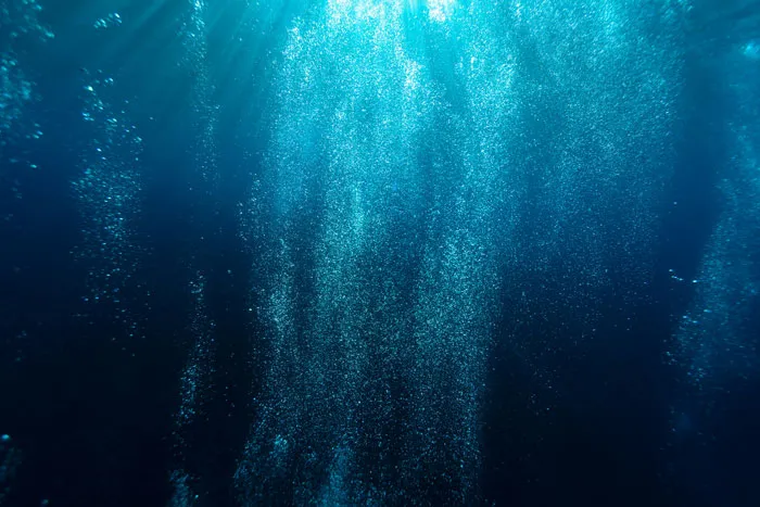 Underwater bubbles rising in deep dark water, illustrating one of the scariest places around the world for brave travelers.