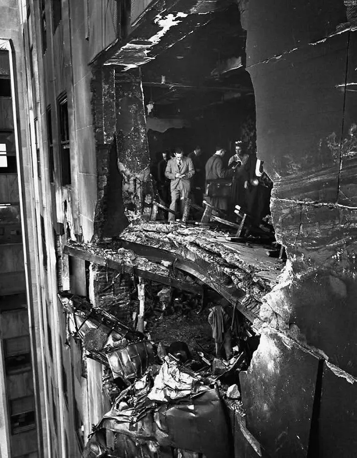Black and white historical photo showing people inspecting severe building damage and debris after a disaster.