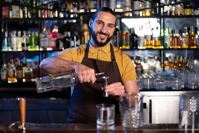 Bartender pouring a drink behind the bar with shelves of liquor bottles in the background during a sour date night.