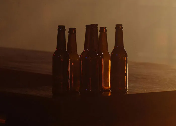 Six empty beer bottles on a wooden table in dim light, symbolizing stories of why people called off their engagements.