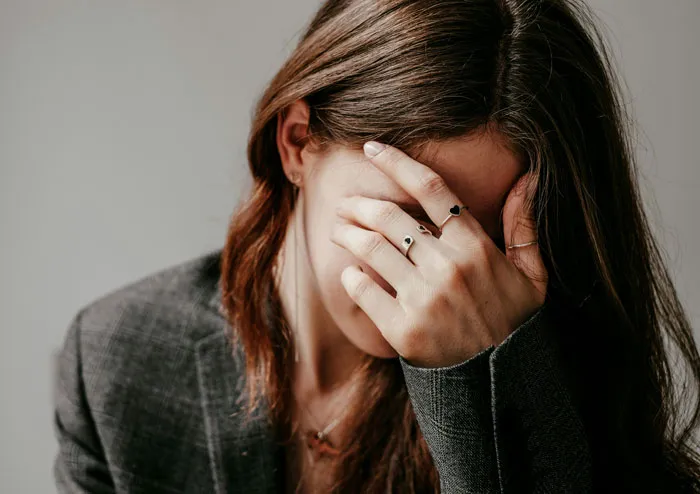Woman in gray blazer covering her face with hand, conveying regret and reflection about biggest mistakes in life.