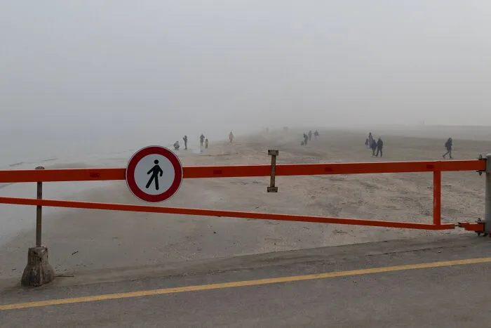 Foggy street scene with pedestrians walking behind a red barrier, captured in a perfectly-timed street photo.