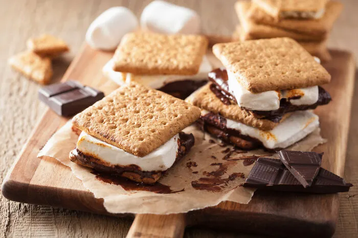 Close-up of American s'mores with melted chocolate and toasted marshmallows on a wooden board, popular American snack.
