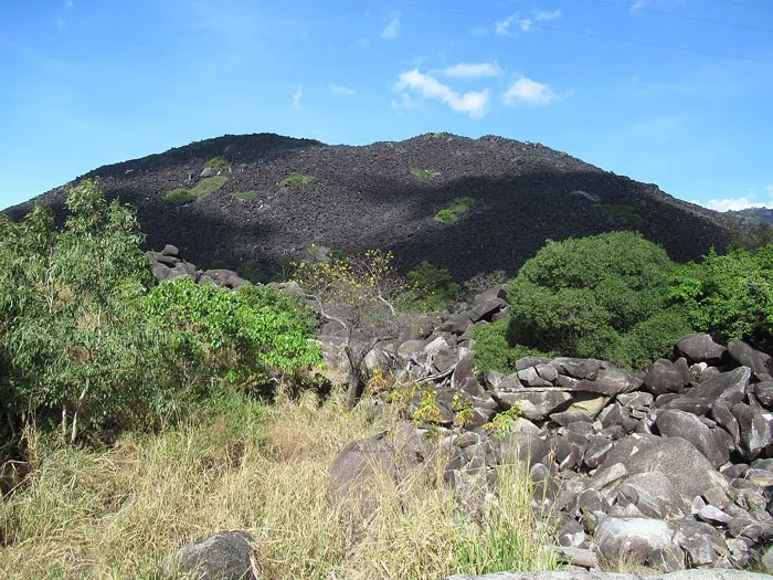 Rocky hill surrounded by vegetation under a clear blue sky, depicting one of the scariest places around the world for brave travelers.