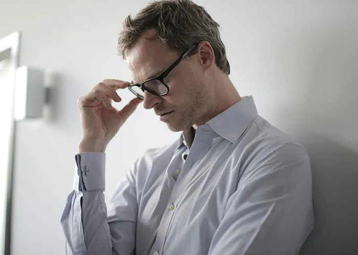 Man in a blue shirt adjusting glasses, looking thoughtful and upset, reflecting on called off engagements and cheating.