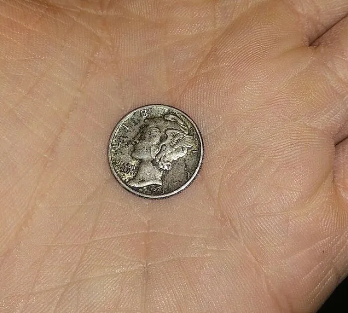 Worn coin held in hand found by abandoned explorers during creepy urban exploration escapades.