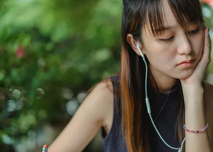 Young woman wearing earphones, looking sad and contemplative, reflecting on engagement and relationship challenges.