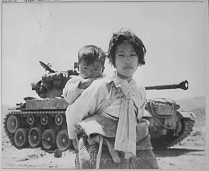 Con su hermano a cuestas, una niña coreana cansada de la guerra camina con dificultad junto a un tanque M-26 atascado, Corea, 1951