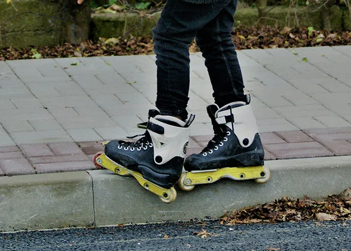 Person wearing black and white rollerblades balancing on a sidewalk curb, showcasing unbelievable experiences in action.