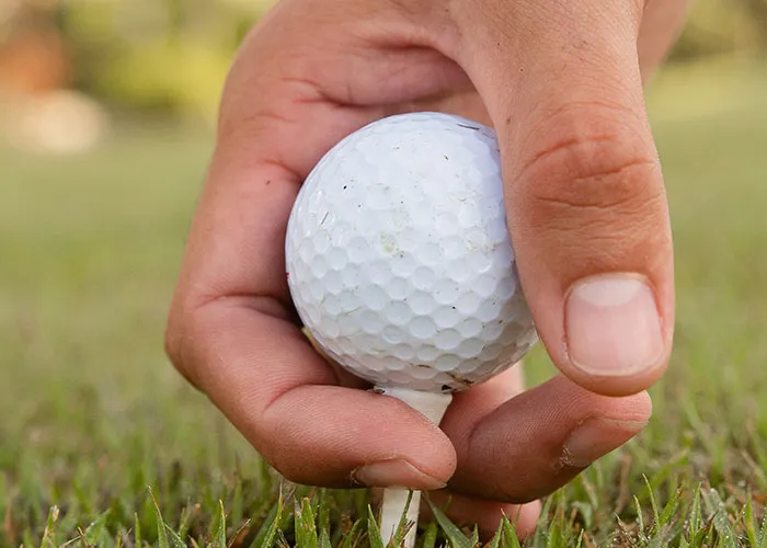 Close-up of hand placing a golf ball on a tee capturing an unbelievable experience in outdoor sports.